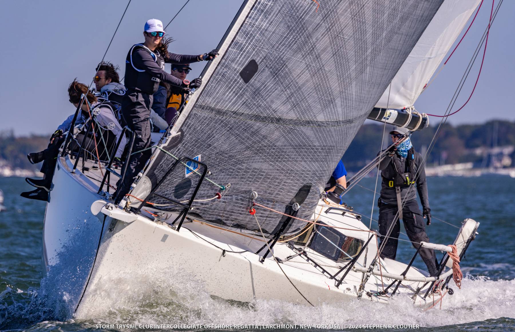 Sailing team members on large sailboat during intense competition.